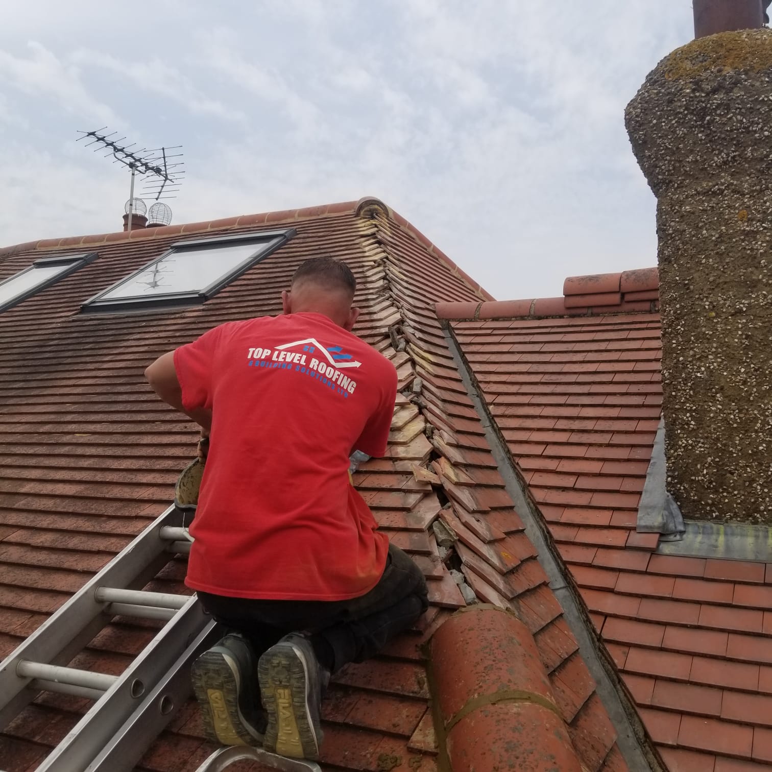 A Top Level Roofing craftsman repairing tiles beside a chimney