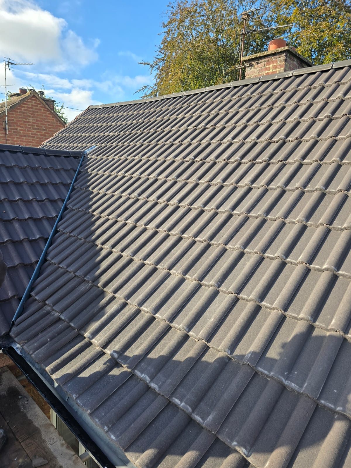 A finished dark tiled roof and lead valley against a blue sky by Top Level Roofing & Building Solutions