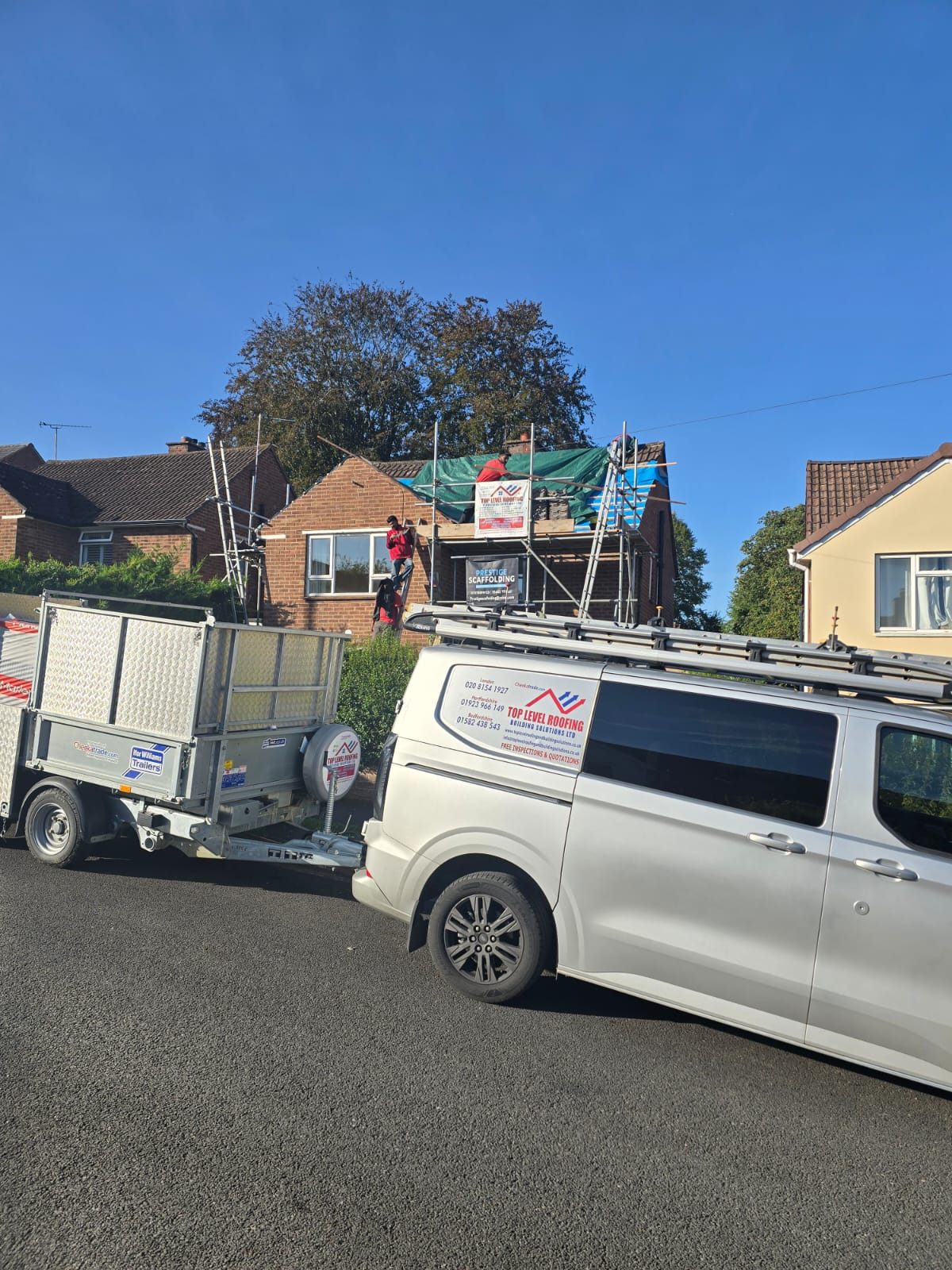 A branded Top Level Roofing van and tipping trailer on site during a re-roof