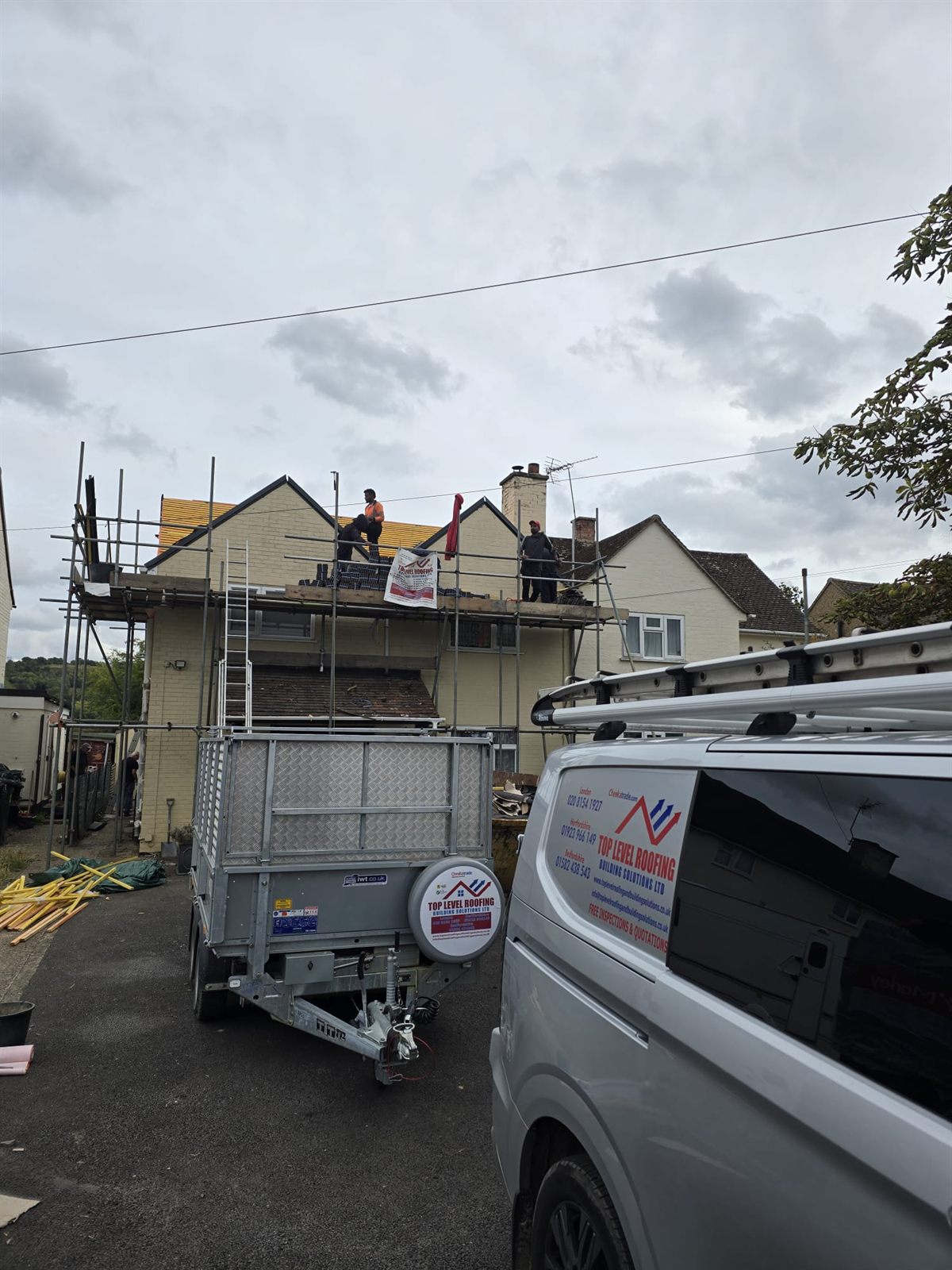 A branded Top Level Roofing van and trailer on site during a re-roof