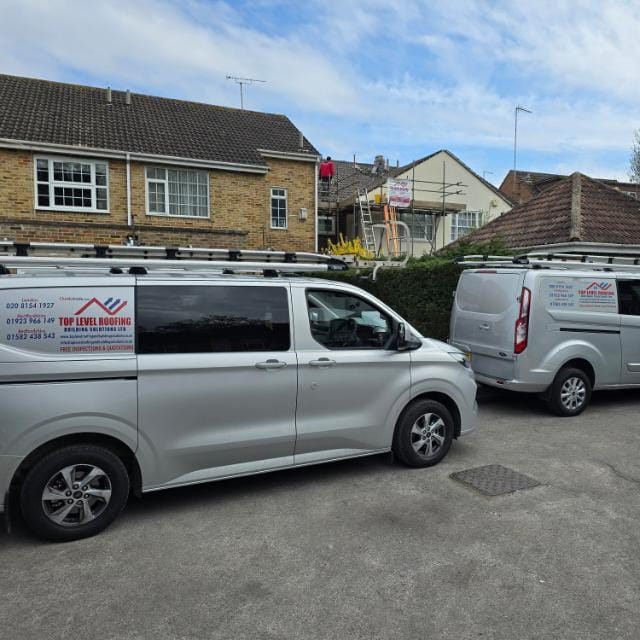 Two branded Top Level Roofing vans parked at a job