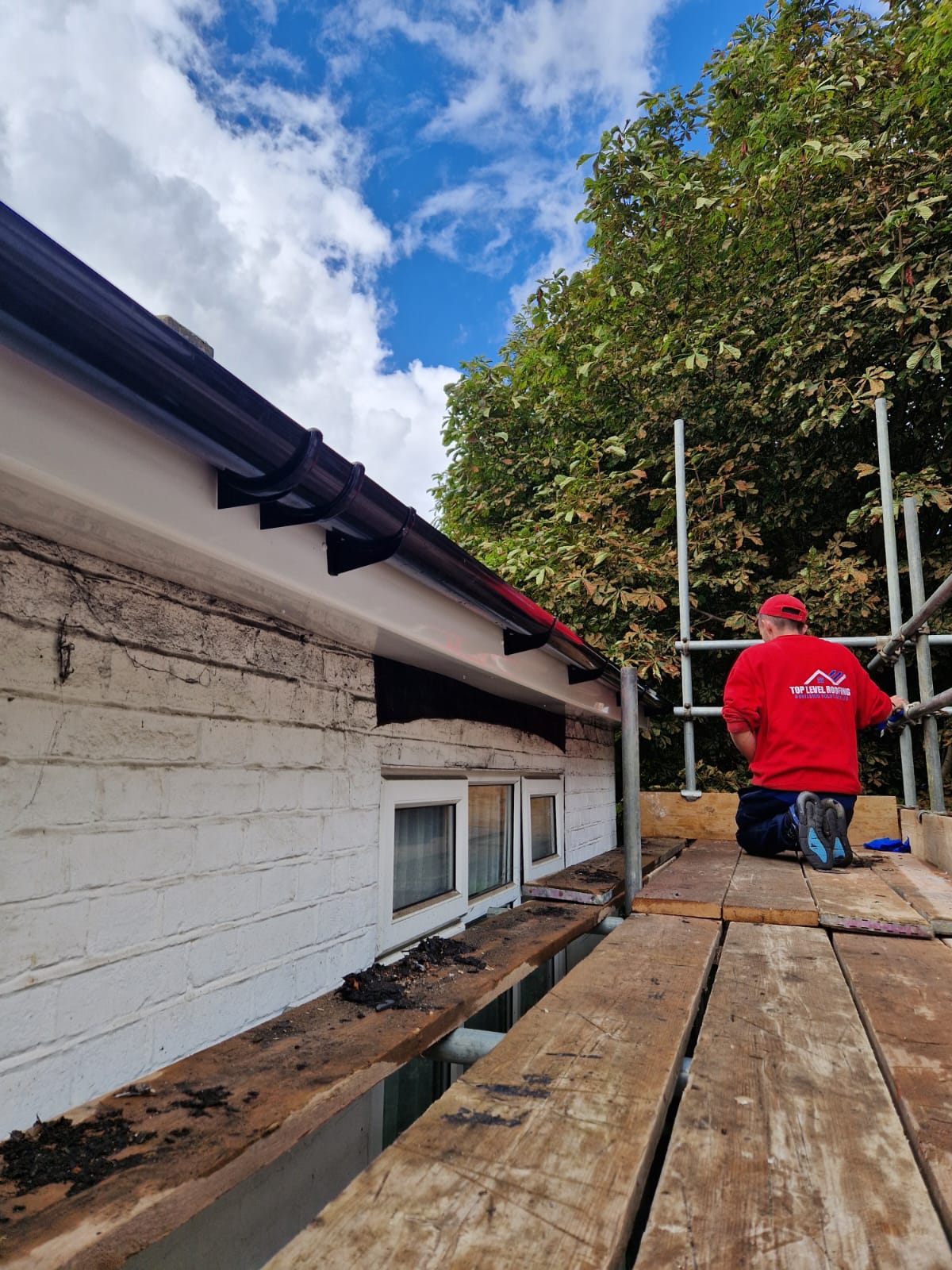 A roofer fitting new black UPVC fascias, soffits and guttering by Top Level Roofing & Building Solutions