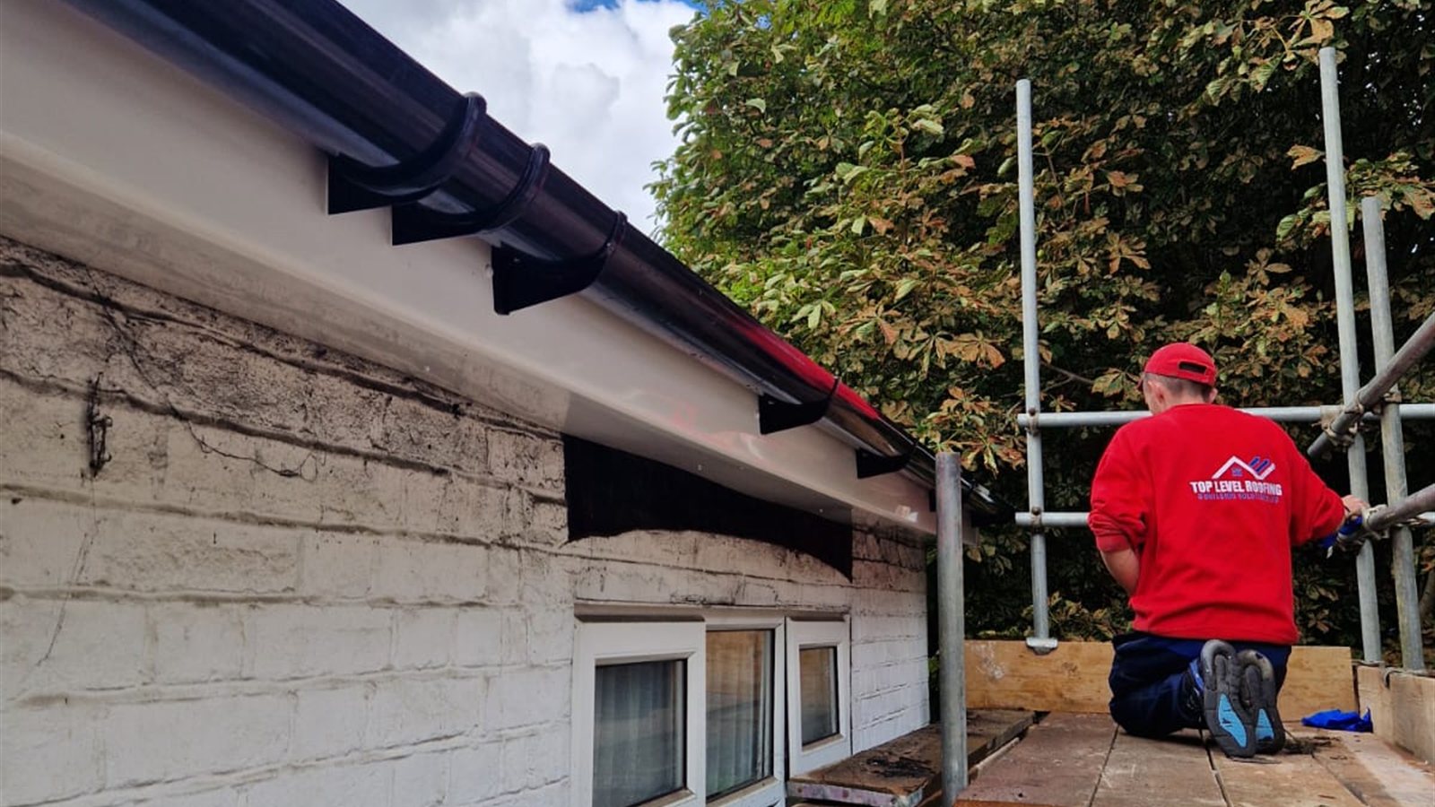 A roofer fitting new black UPVC fascias, soffits and guttering